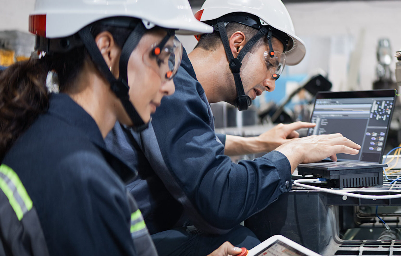 White Latin industrial engineer man, woman work together operating electric machine in robotic factory. Mechanical industry engineering business. Blue collar worker, technology job lifestyle concept