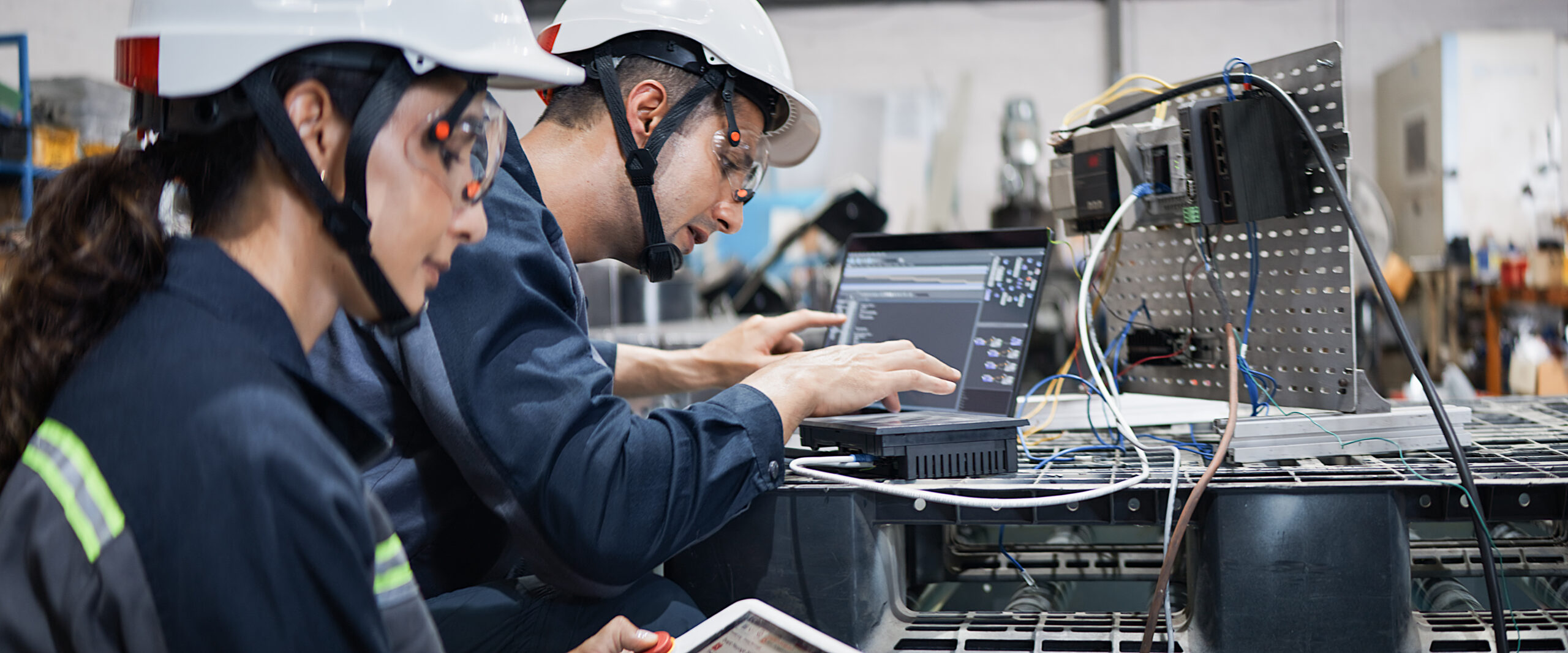 White Latin industrial engineer man, woman work together operating electric machine in robotic factory. Mechanical industry engineering business. Blue collar worker, technology job lifestyle concept