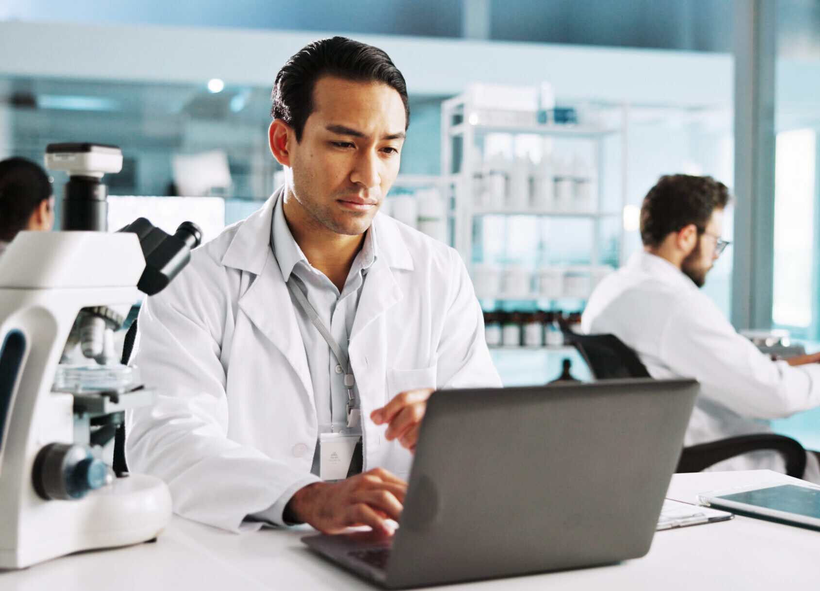 Laptop, science and study with man in laboratory for healthcare, medical or pharmaceutical innovation. Computer microscope and online research with scientist in clinical trial for development